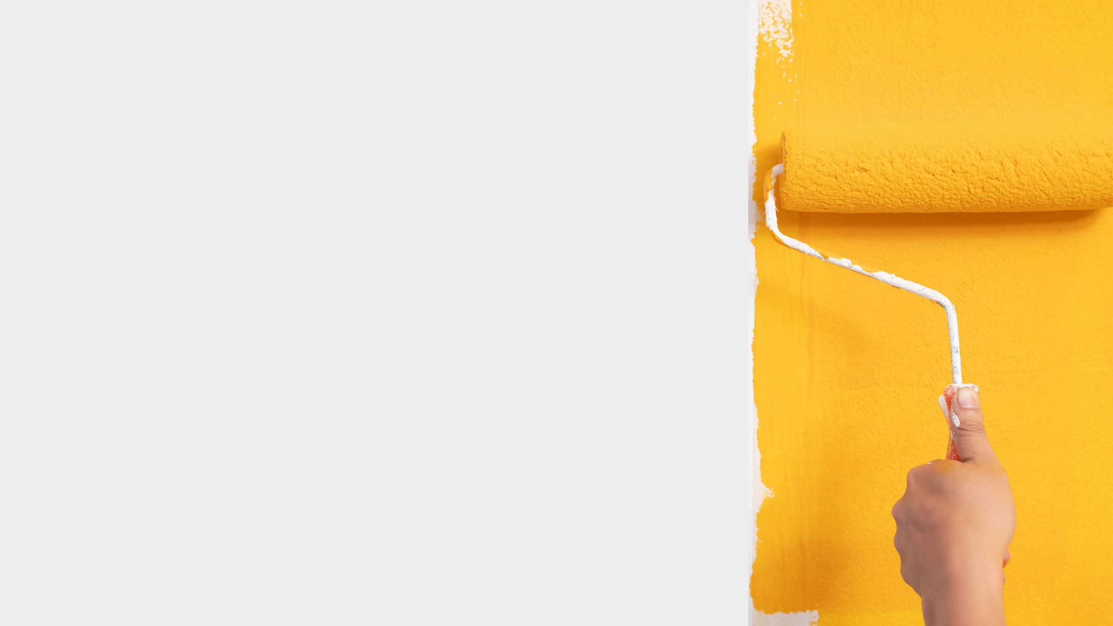 Hand using a paint roller to apply bright yellow paint on an interior wall, showing smooth coverage and technique for Denver home painting projects